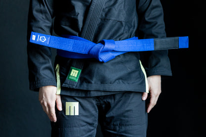 Person wearing a black martial arts uniform with a blue belt on a dark background