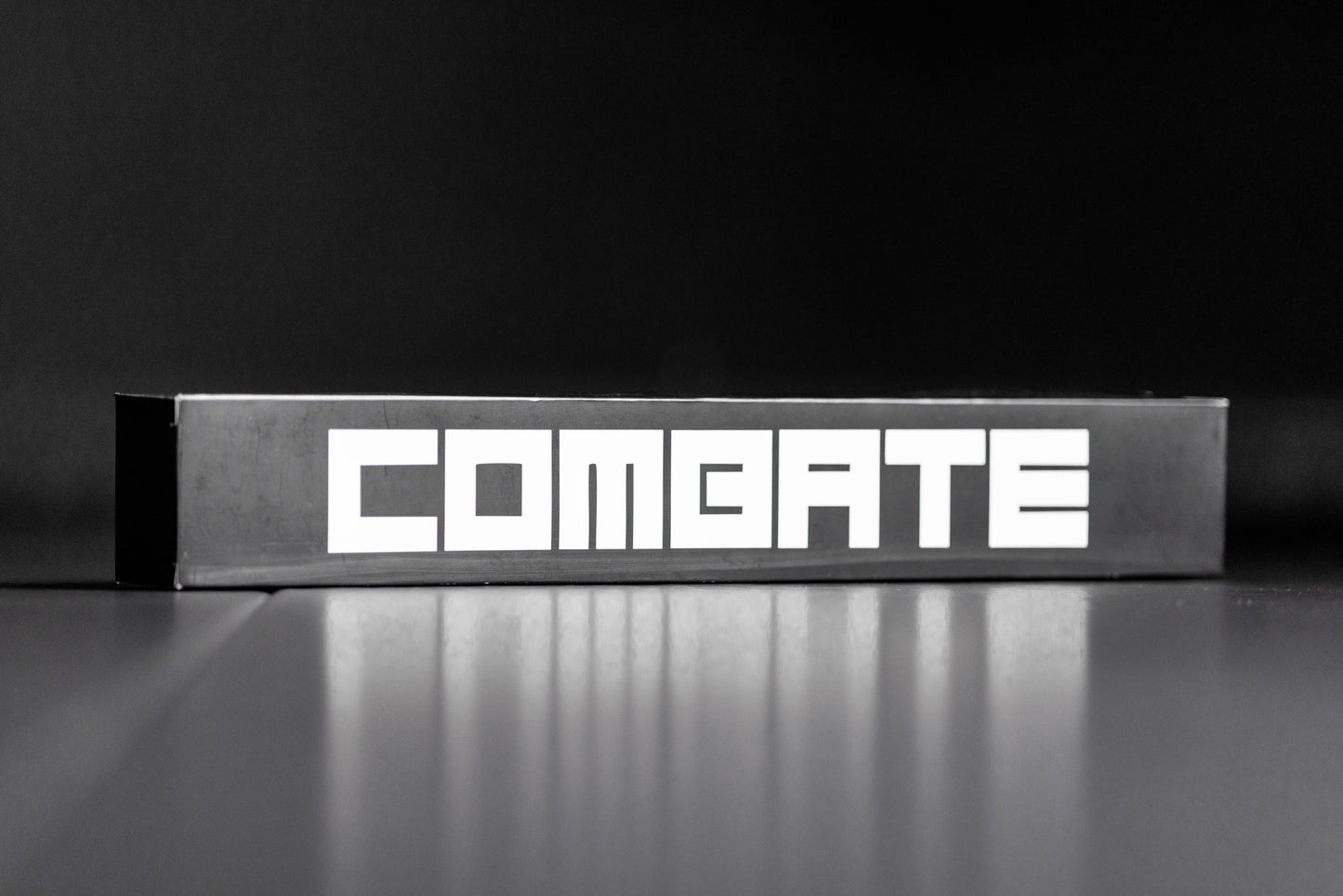 Metallic box with 'COMBATE' branding on a reflective surface and black background