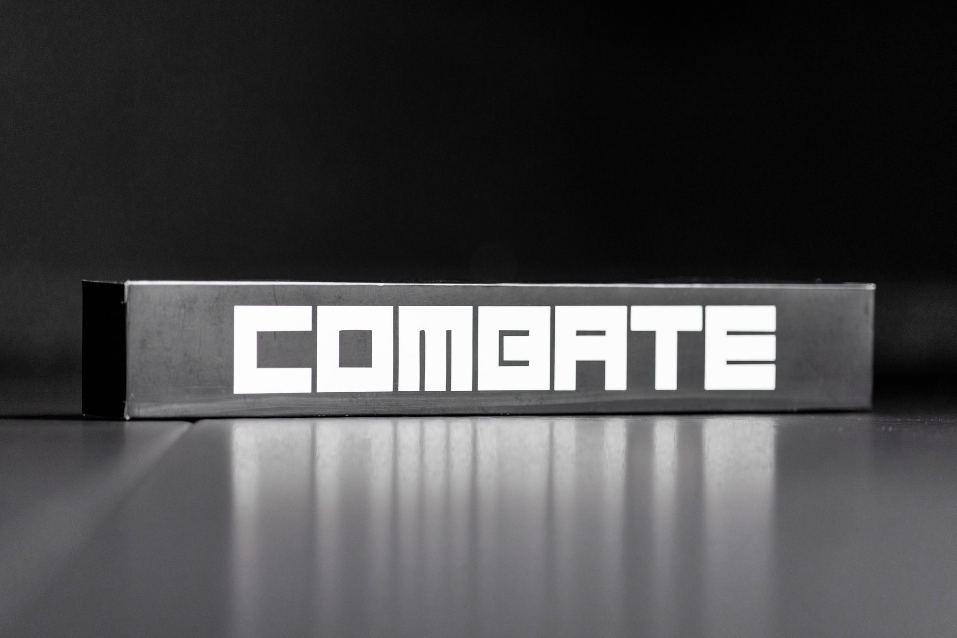 Metallic box with 'COMBATE' branding on a reflective surface and black background
