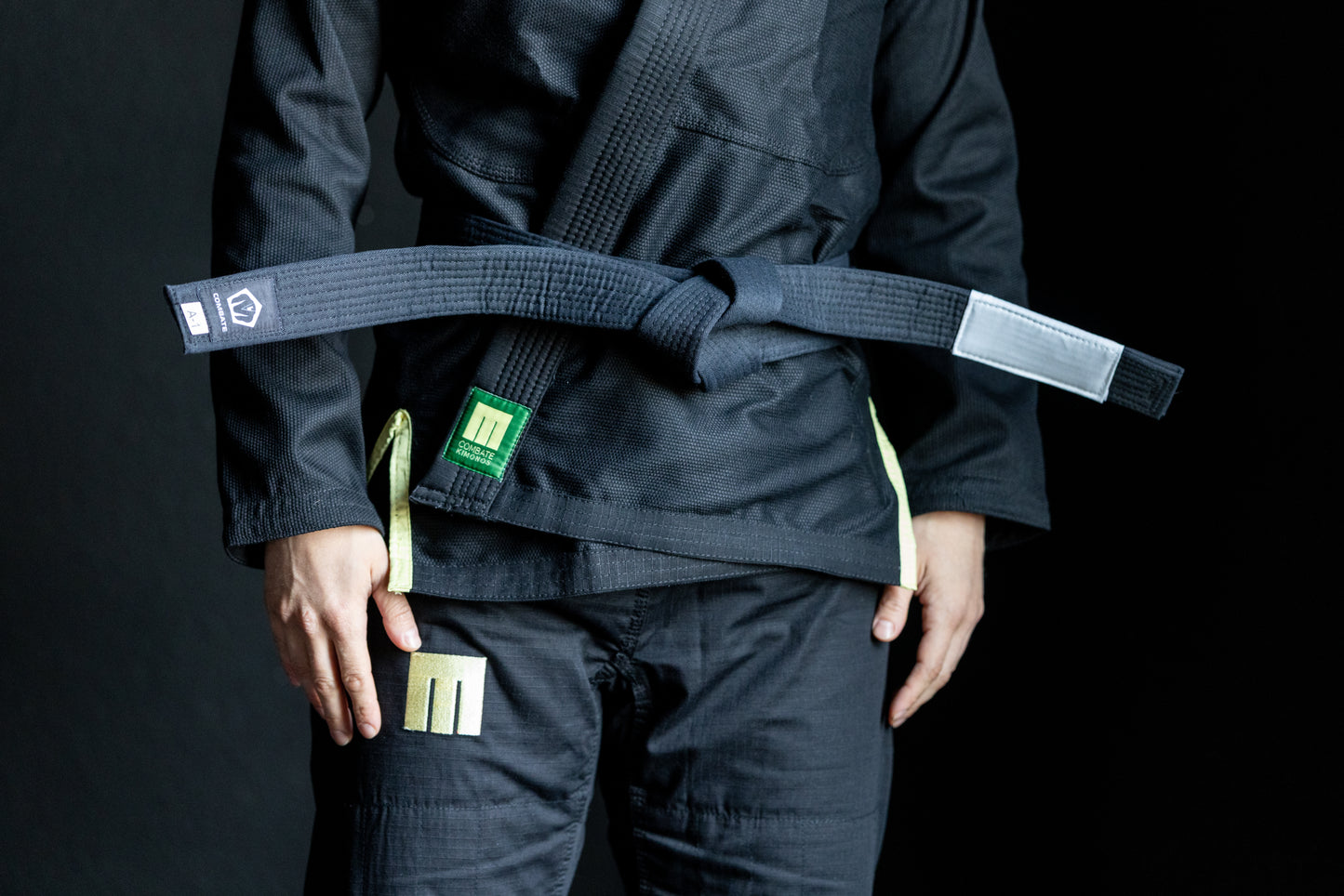 Person wearing a black martial arts uniform with a green belt on a black background