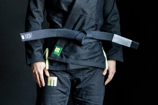Person wearing a black martial arts uniform with a green belt on a black background