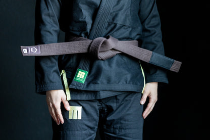 Person wearing a black martial arts uniform with a brown belt on a dark background