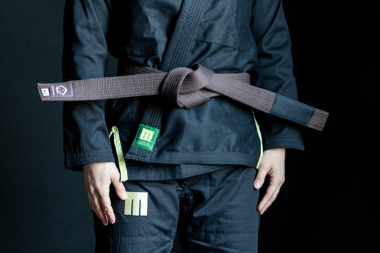 Person wearing a black martial arts uniform with a brown belt on a dark background