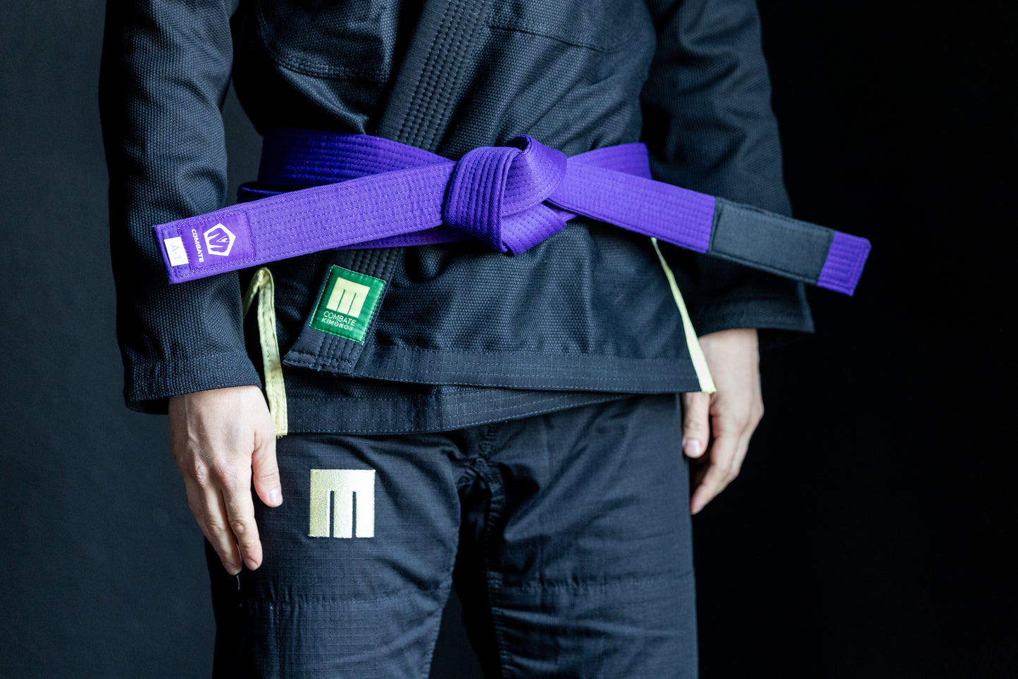 Person wearing a black martial arts uniform with a purple belt on a dark background