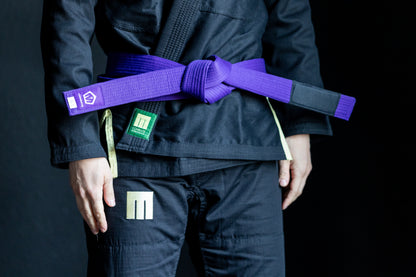 Person wearing a black martial arts uniform with a purple belt on a dark background
